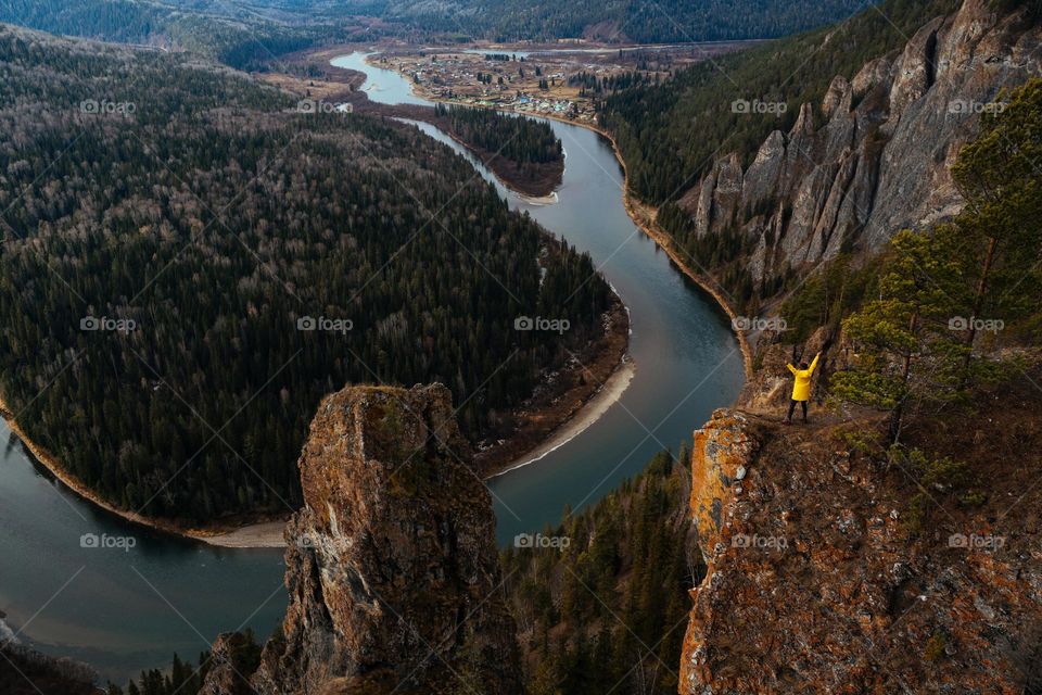 Person in yellow raincoat standing on the top of the rock. Breathtaking river view. Hiking and trekking. Scenic landscape. Inspiring moments