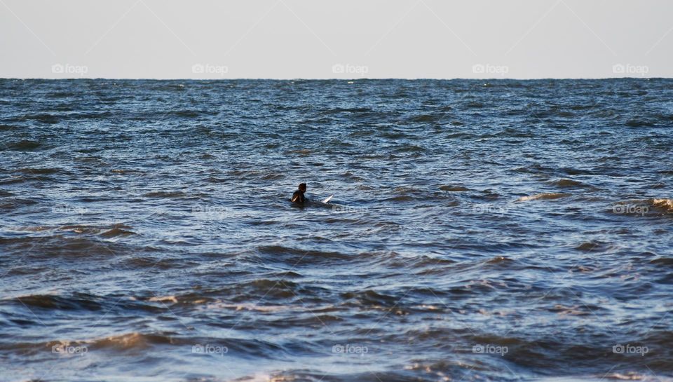 A surf enthusiast's makes his way out to the Atlantic to get some practice in catching waves in the dusk of day at Virginia Beach.