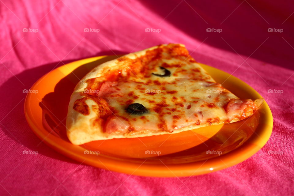 Slice of pizza in a orange plate on a pink background