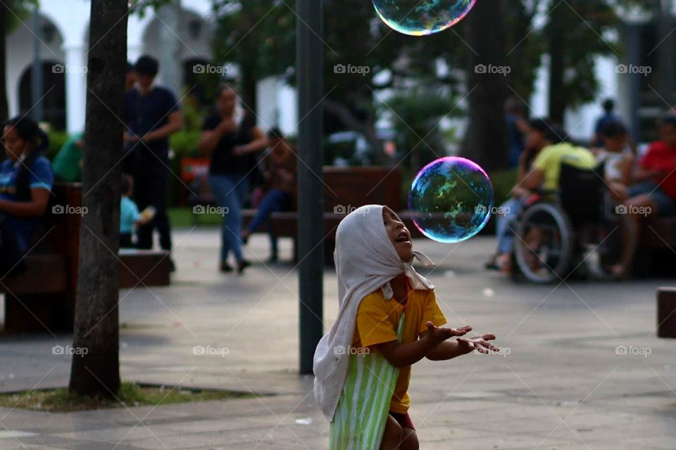 Happy little boy is playing with a soapy bubble on a town square in Bolivia