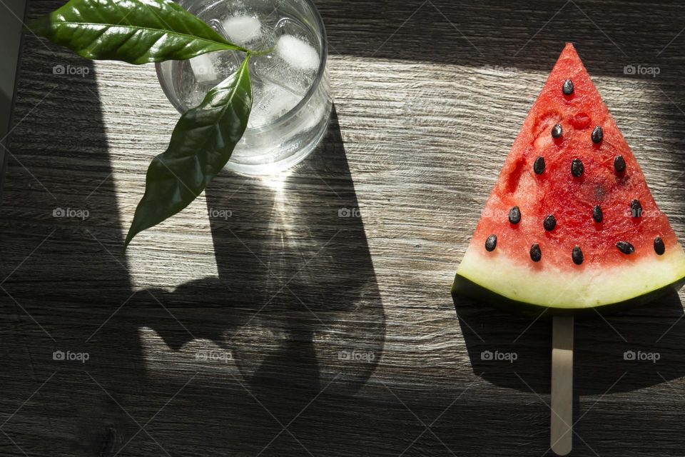 Cold, transparent drink with ice in a glass glass with summer snacks on a wooden background.