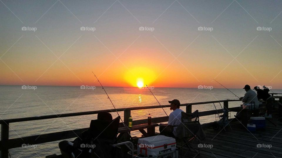 People fishing on sea during sunset