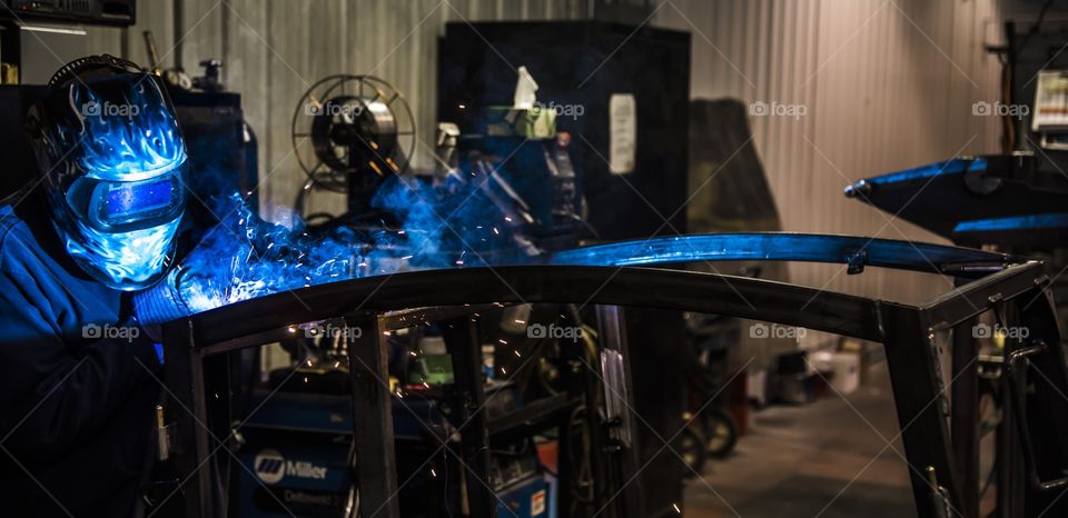 This welder is building a frame by welding bar steel together using fixtures to produce a ROPS frame for a heavy equipment Cab. 