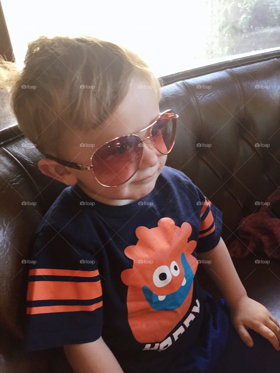 A cute little two year old boy wearing oversized aviator sunglasses. 
