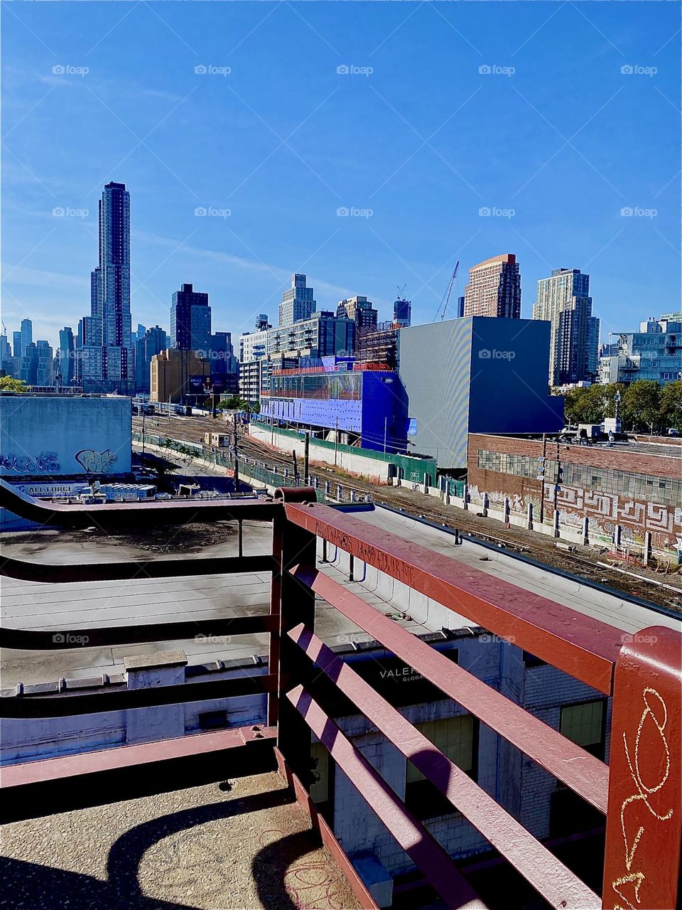 We have arrived at the top of the staircase of the „Pulaski Bridge“ and are overlooking LIC, Queens. The red parallel bars of the railing are accentuated by the shadows they cast and those being cast onto them. 2023. Hypnotic Productions