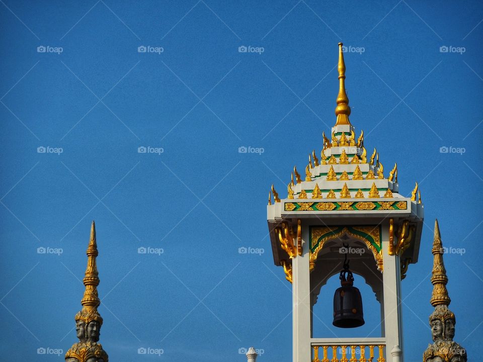 A hanging bell and Buddhist sculpture inside a temple with blue sky background.
