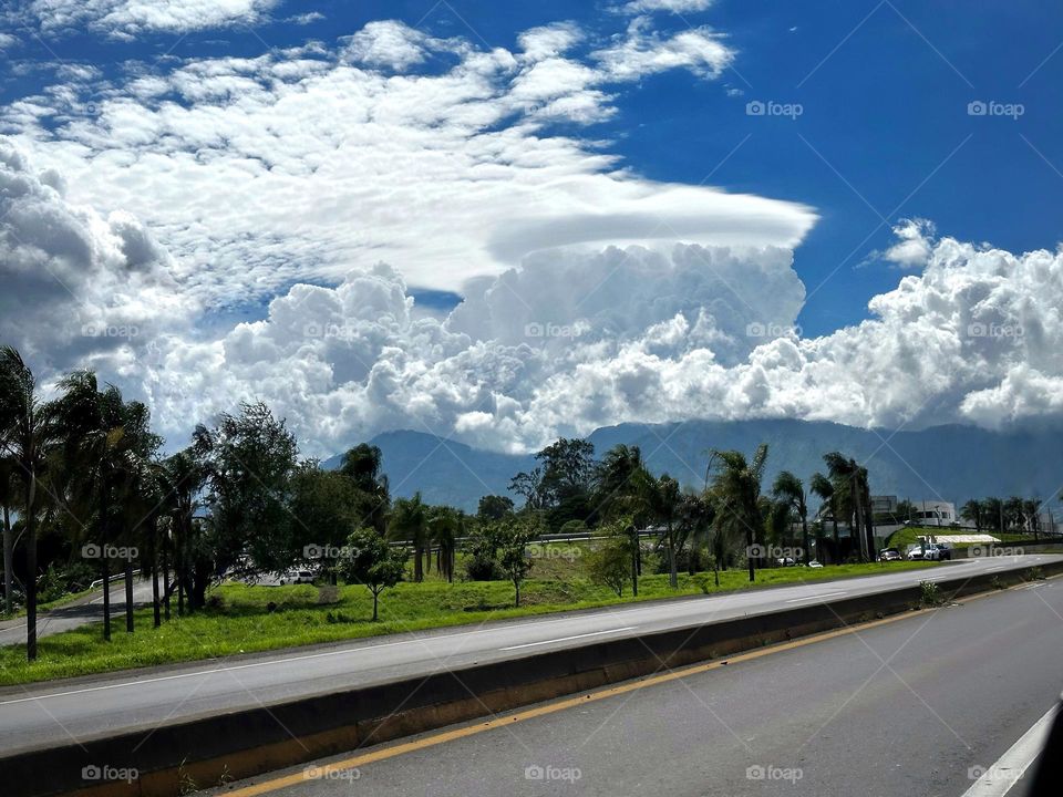 Dramatic clouds blowing up behind the mountains with a road in the scene.