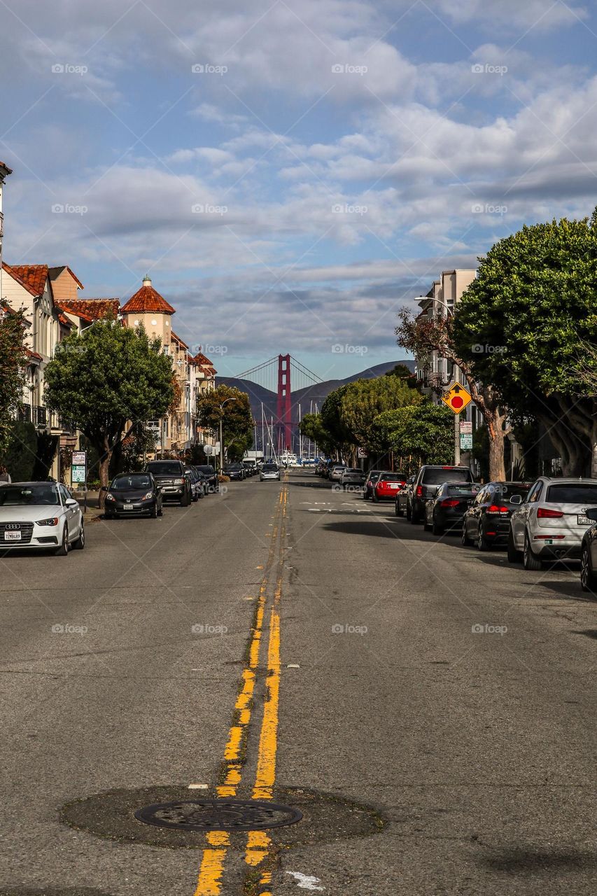 View down Cervantes Street in San Francisco California in the Marina District, looking at the Golden Gate Bridge on a beautiful day with some clouds in the sky
