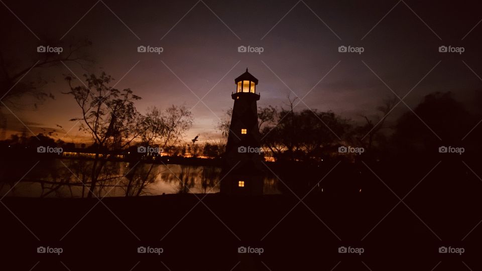 Lake Shore Lighthouse just before Night. Reflections of distant Shore Line, Distant Shore Lighting Reflective on Top of Lake Waters Captivating the Night.