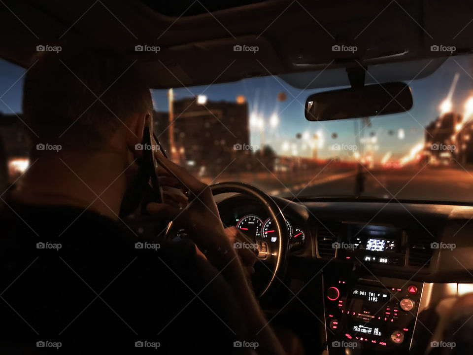 Young man using mobile phone while driving a car through the night city 