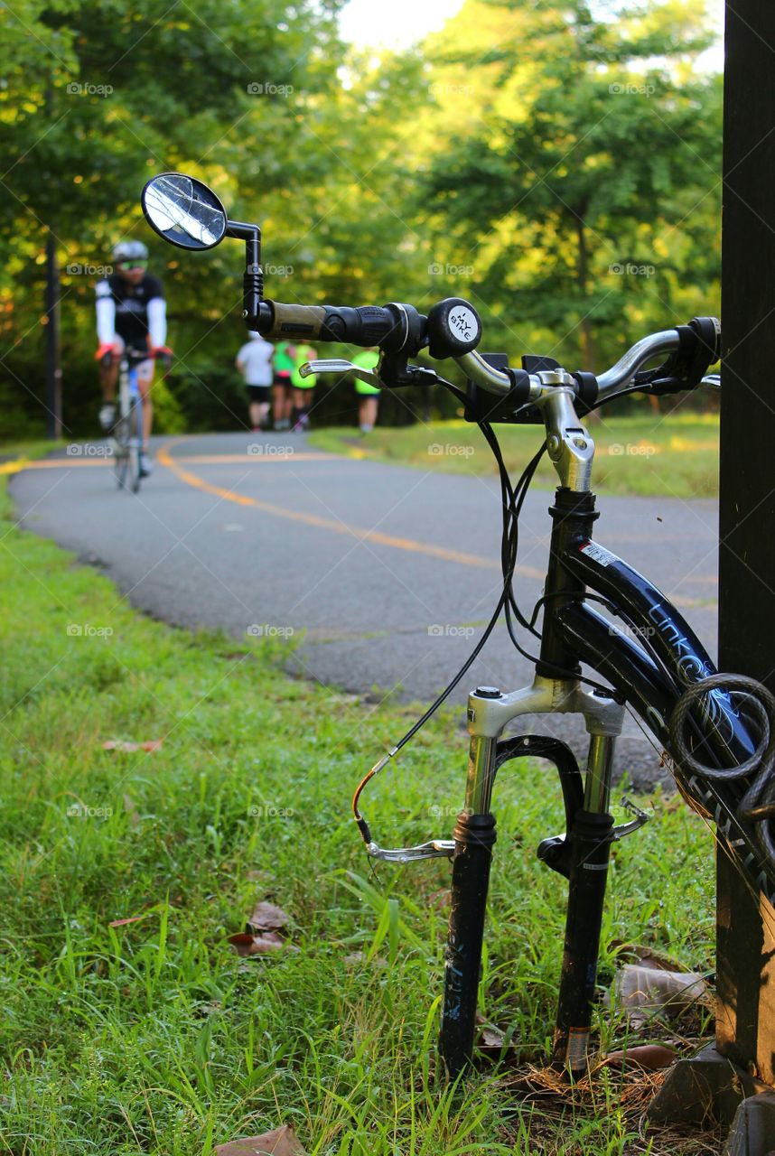 Abandoned, stripped bicycle chanined to lamppost with bicyclist and joggers in the background