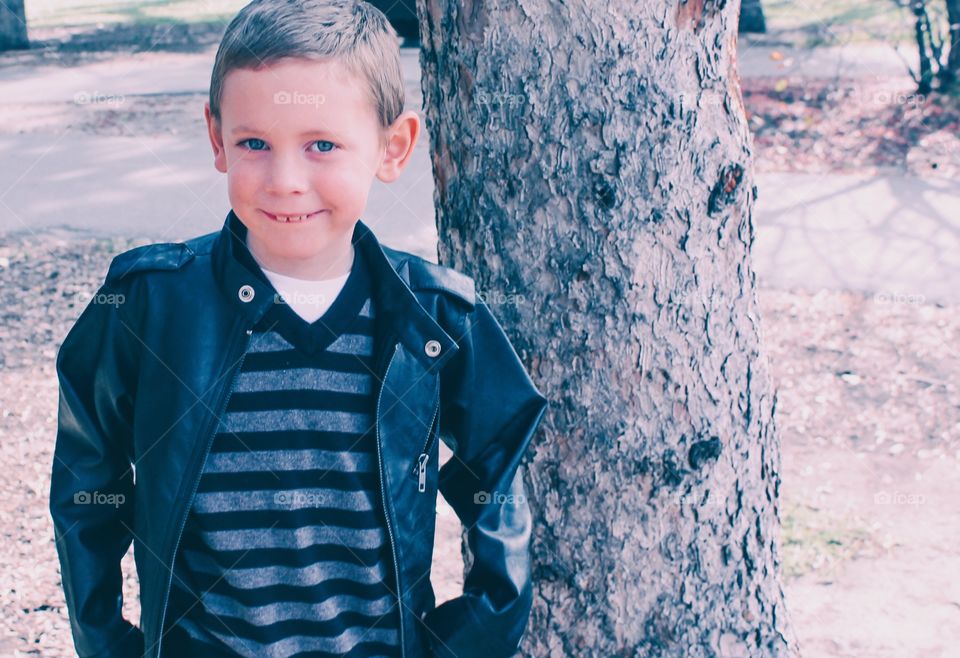 Look at this handsome young boy posing by a tree in the park 