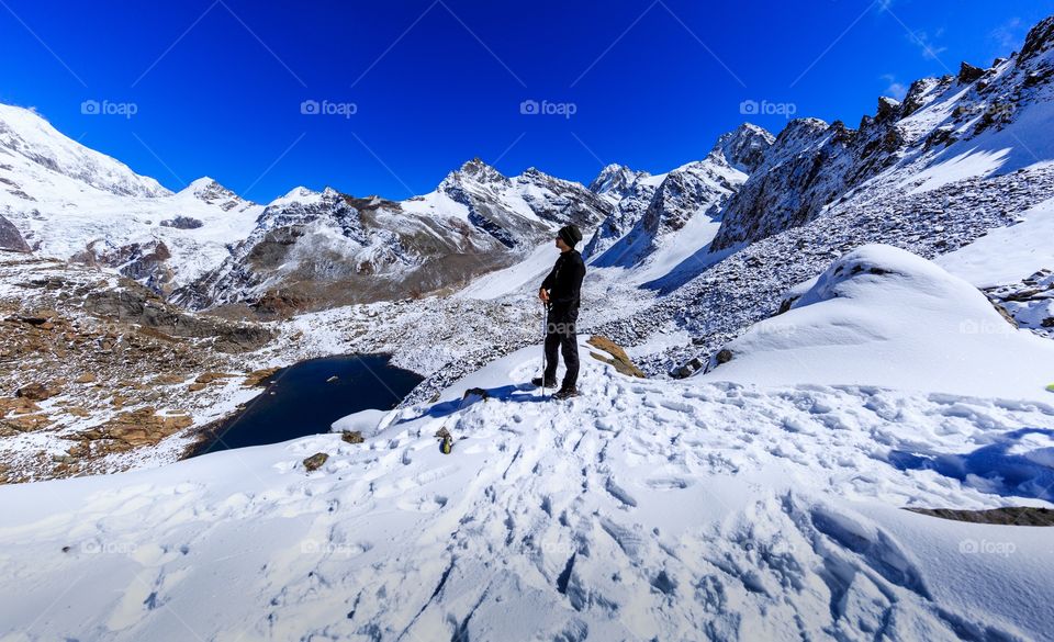 wanderlust trekker standing surrounded by snow capped mountains and blue sky