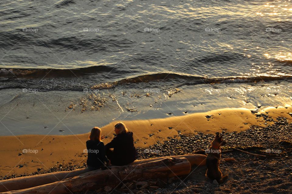 Couple sittin on a long by the ocean on sunset 