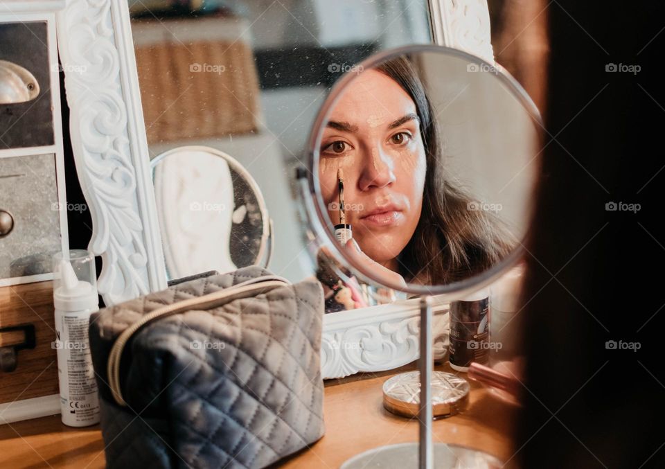 Mirror photo of woman applying foundation makeup on her face