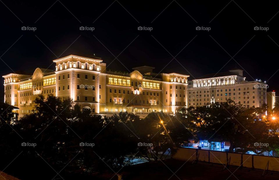 big city building with warm lights glowing bright behind a blue and green bus depot all against a deep dark sky