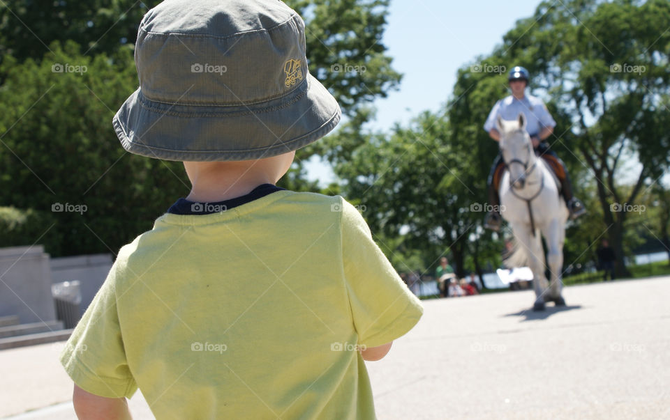 Rear view of a boy looking at police man riding horse