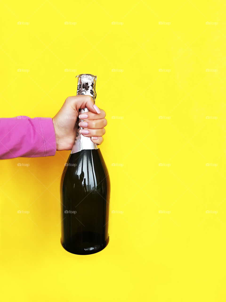 Bottle of champagne in hand on yellow background 