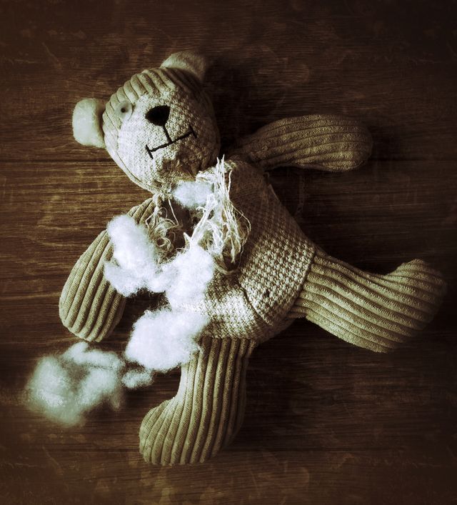 An old, abandoned teddy bear with his stuffing pulled out and laying, helpless on a wooden floor.