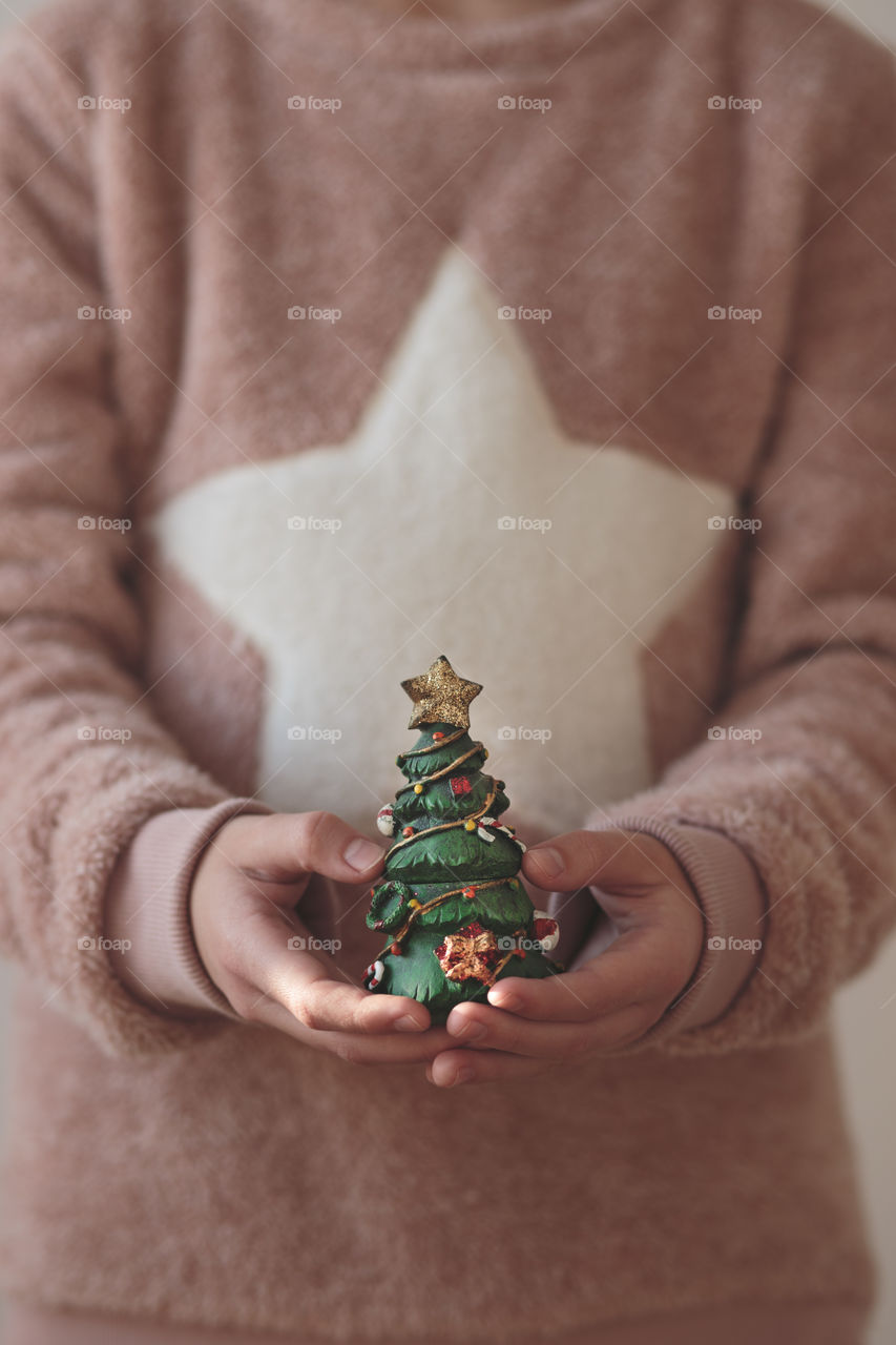 Close shot of young girl wearing warm sweater holding Christmas tree figurine