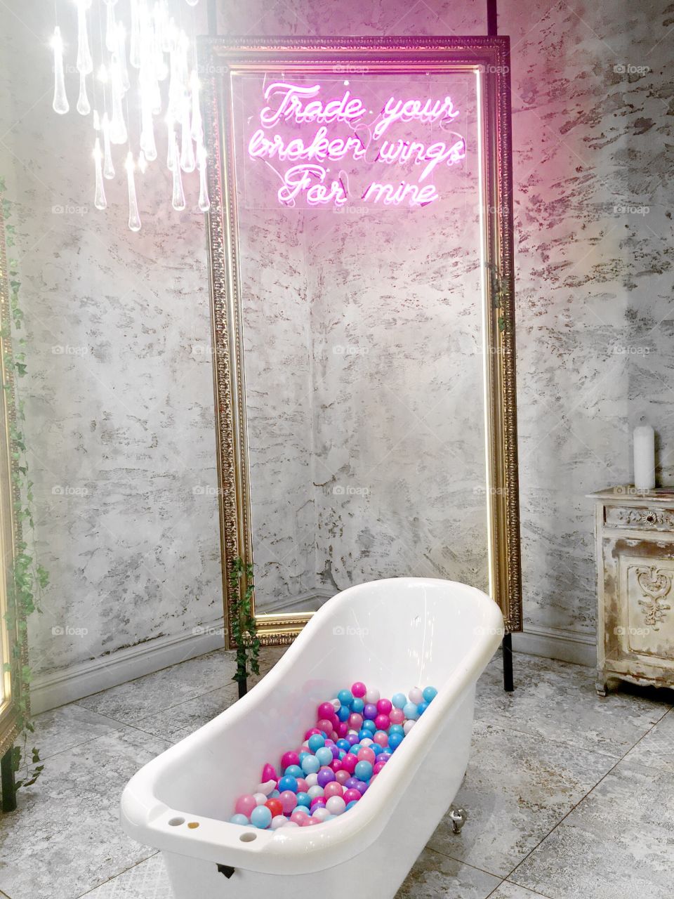 A bath bull of coloured balls, golden frame and pink neon lighting with an inspirational message “trade your broken wings for mine”