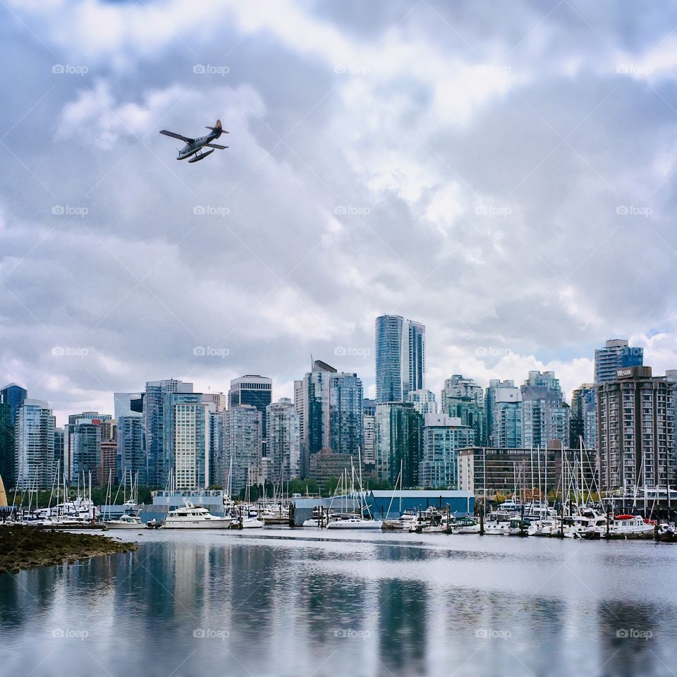 A small plane flies over the waterfront in Victoria, British Columbia. Calm water reflects the cityscape 