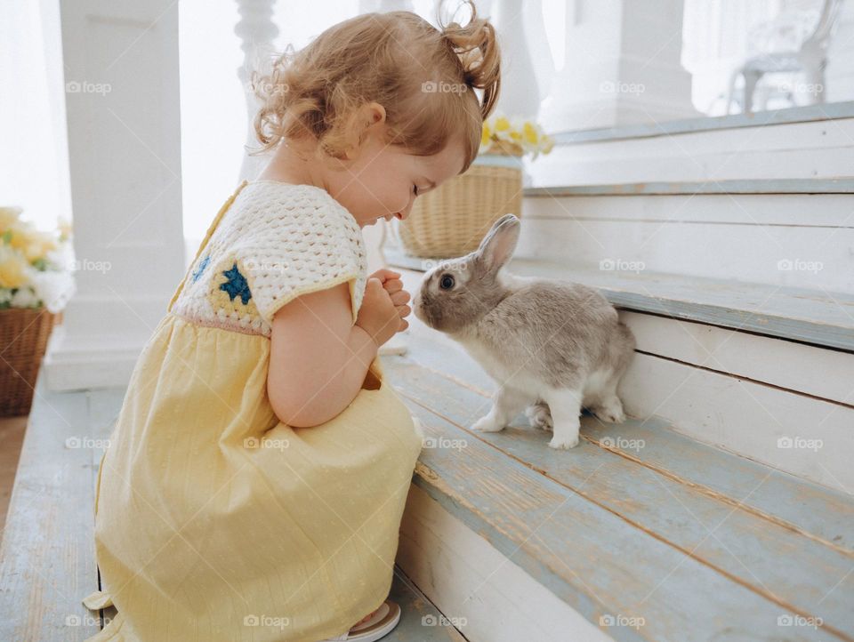 Small girl in yellow dress play with rabbit