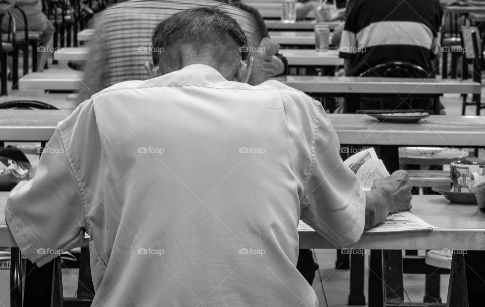 Old man sitting to read newspaper at food center