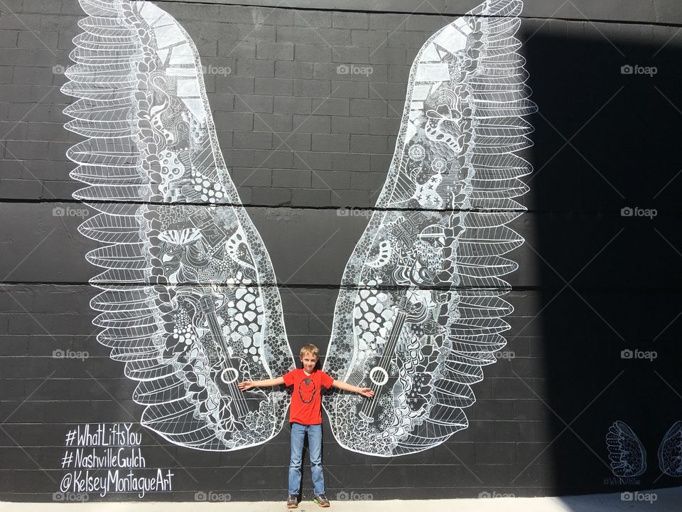 Boy leaning against big white wings on wall