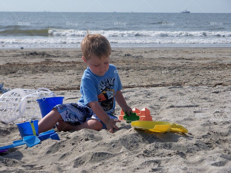 Blonde boy playing toy on sand at beach