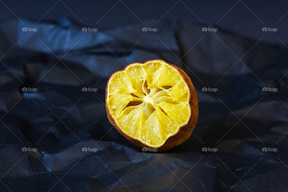 Ugly organic lemon. Deformed half of a lemon with old flesh with damaged, rotten ugly peel on a black crumpled paper background with large creases. Horizontal orientation. Organic waste