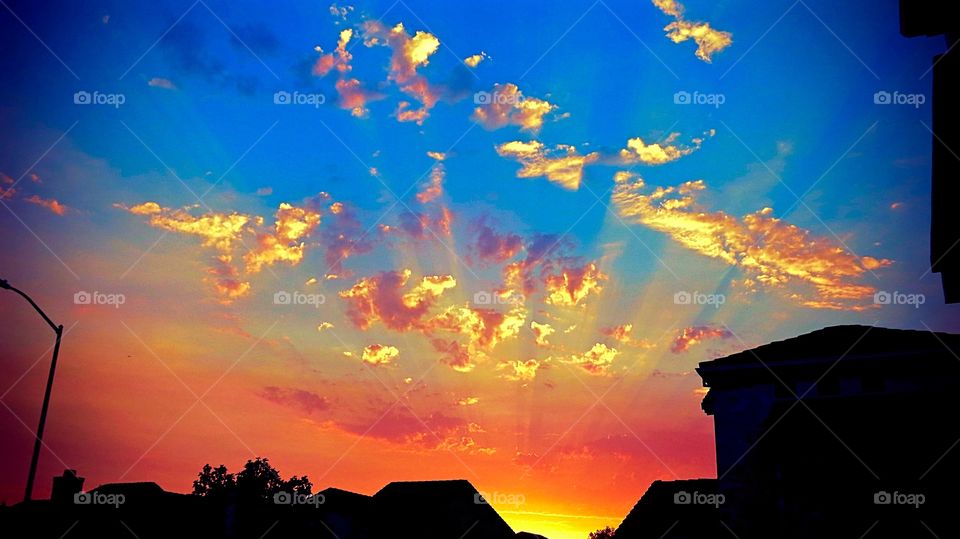 A colorful sunset silhouetting the roofline of houses.