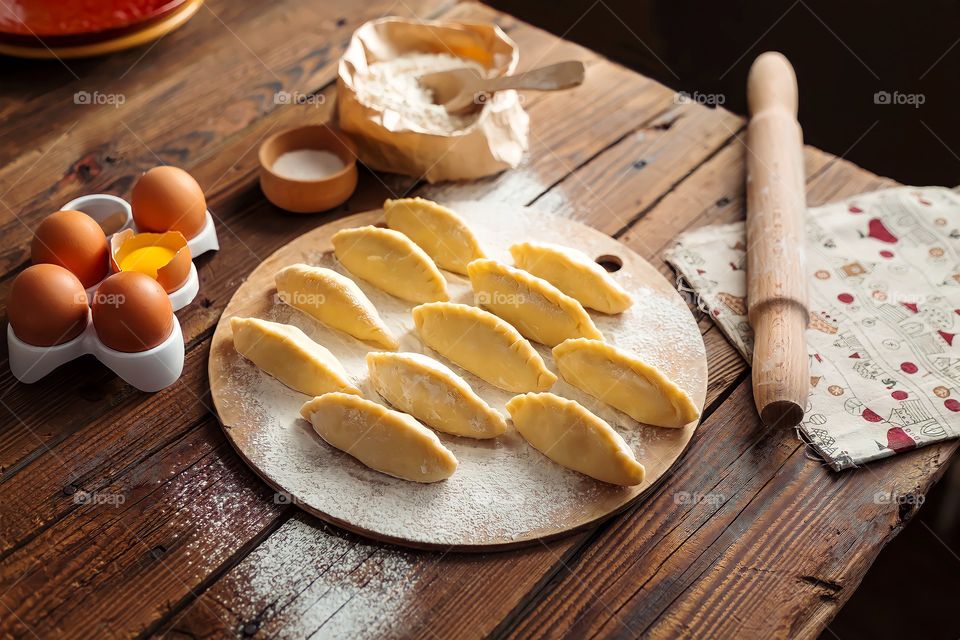 Close up Russian pirozhki baked patties ready to be baked surrounded with eggs, flour and other ingredients.