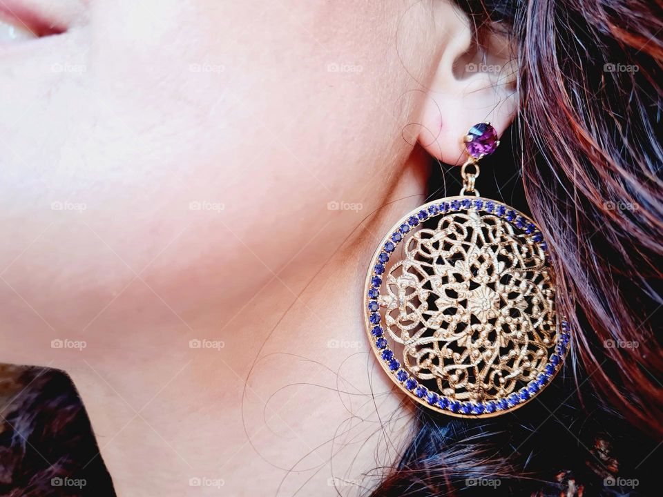 detail of gold earring with purple rhinestones worn by a woman with curly hair