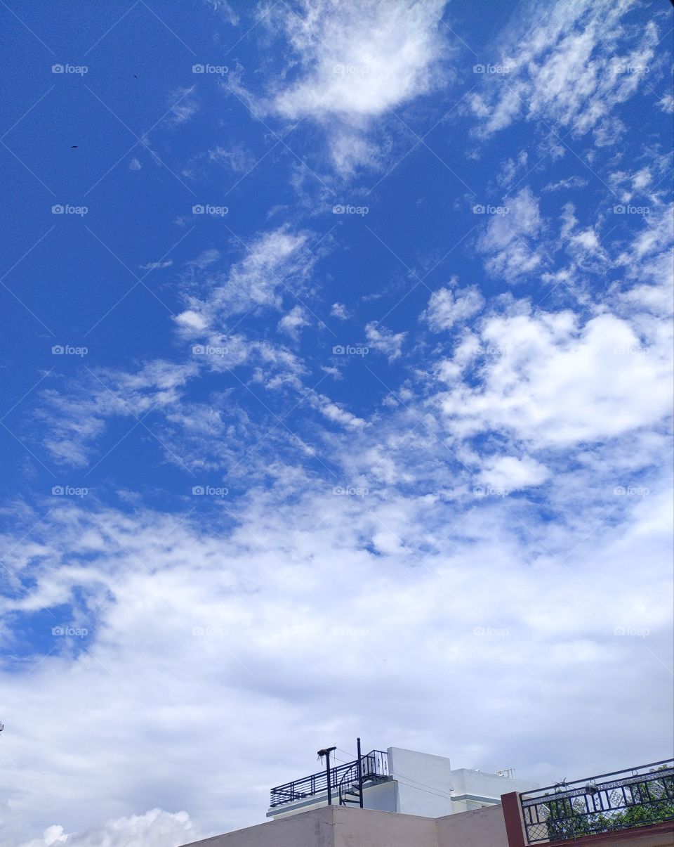 Flakes of white clouds floating across a beautiful blue sky over Mussoorie hills