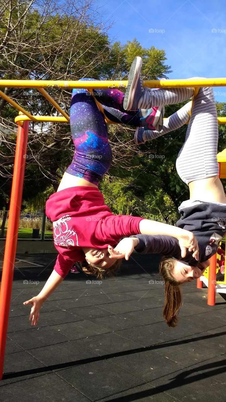 two girls hanging on a climbing frame upside down laughing