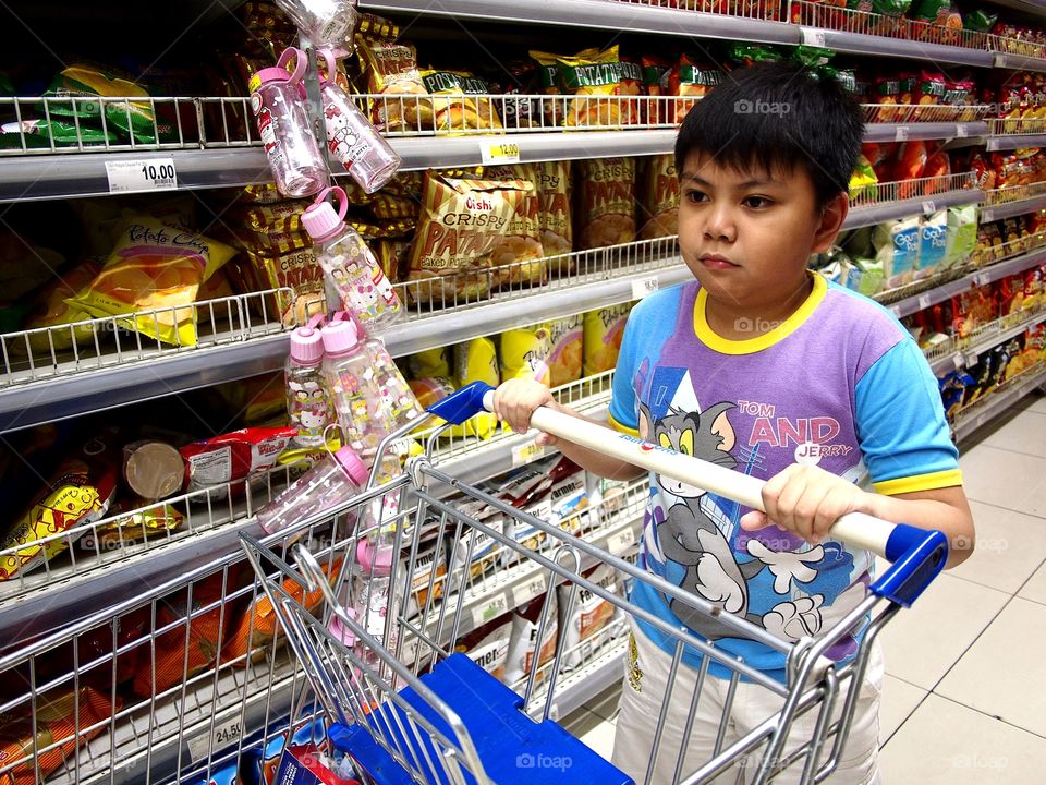 a young boy pushes a grocery cart inside a grocery store