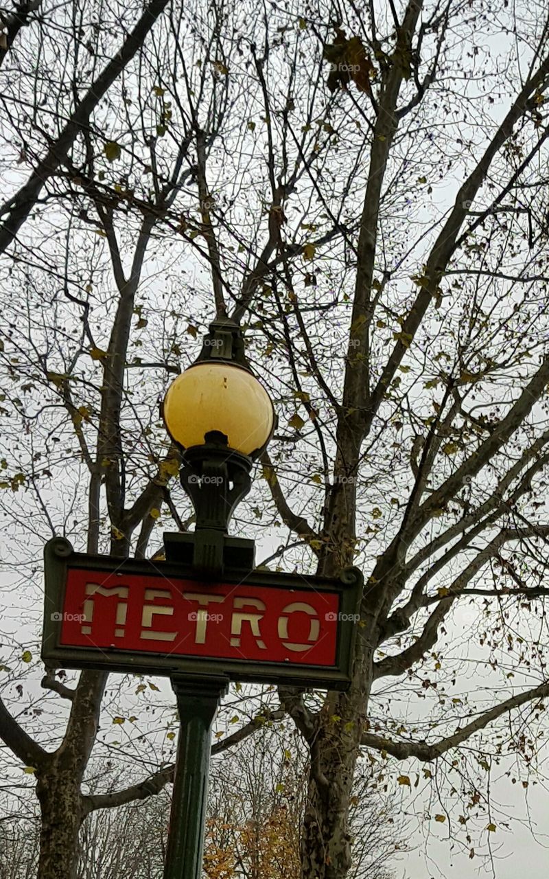 Old vintage metro sign with street lamp in Paris France with winter sky and bare tree branches behind