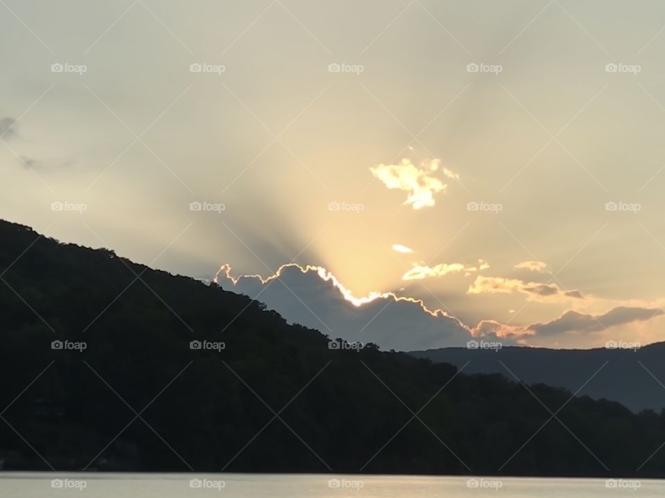 Sun rays shining from behind cloud over mountains and river