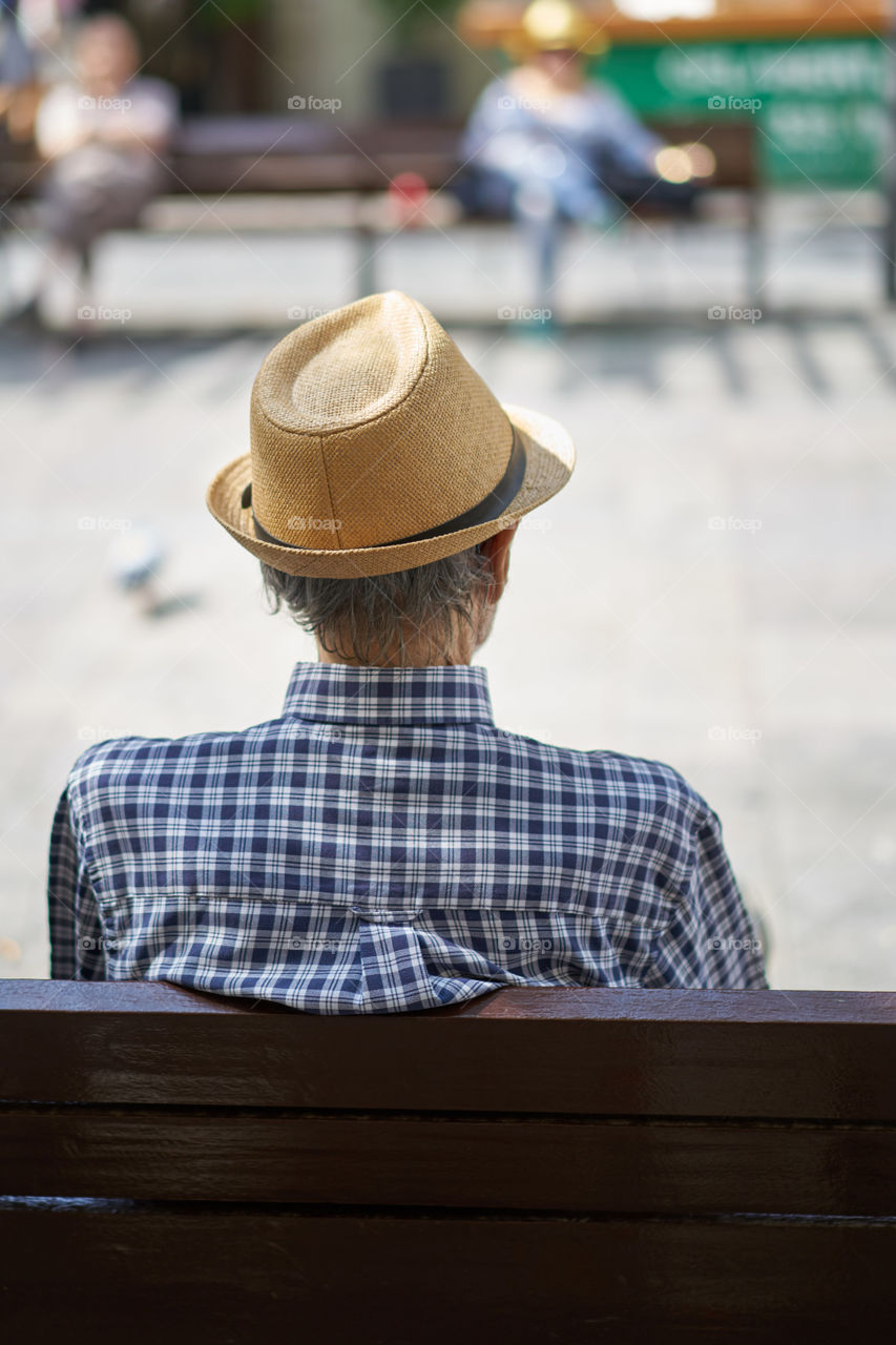 Elderly man with hat sitting in a street bench