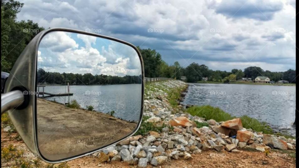 Sideview from rearview truck mirror of lake, rocks, water, clouds