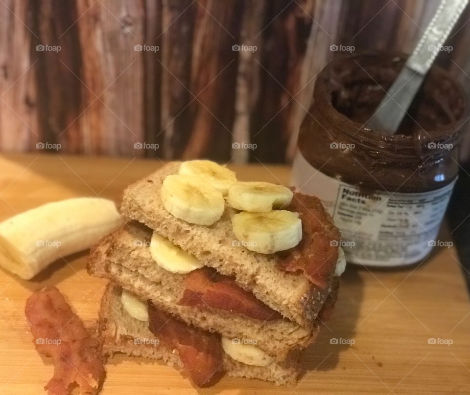 A yummy chocolate Nutella, bacon and banana sandwich on display on a cutting board against a wooden background. USA, America