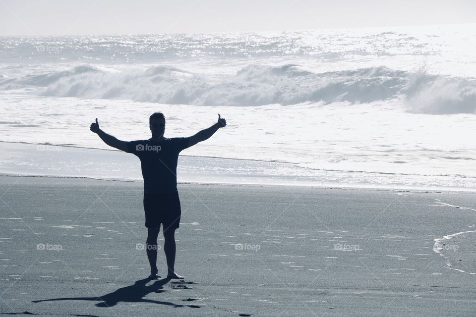 Silhouette of a young man praising the enormous power of the  ocean sparkling on a sunny beautiful day