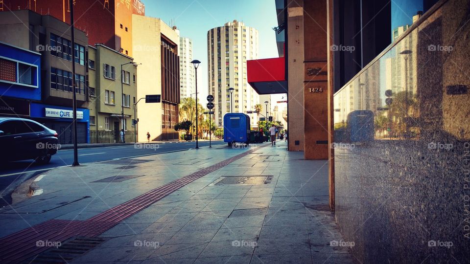 Calçada brilhante lisa, rua, veículos e prédios.