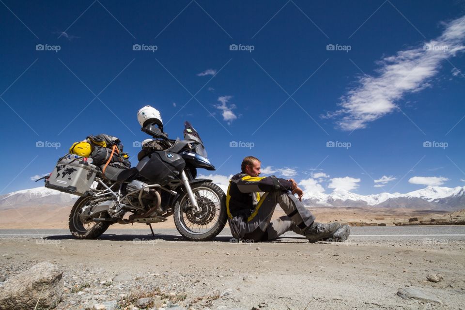 Motorcycle and rider. Motorcycle and rider having pause in  western China. Himalaya maintains in the background. Few clouds in blue sky