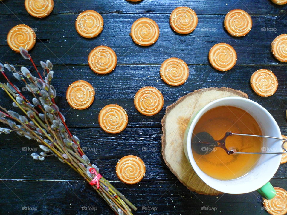 cookies, a cup of tea and willow branches on a black background