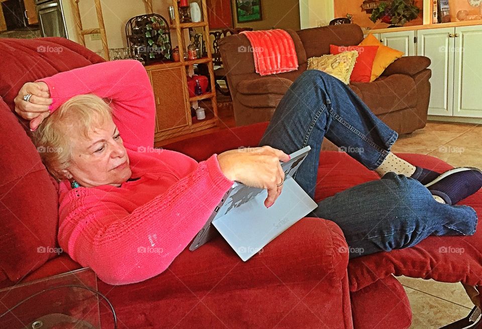 Mature woman lying on sofa looking at digital tablet
