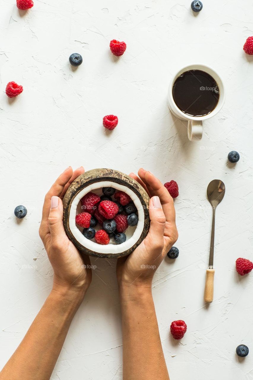 Hands holding coconut bowl with fresh berries 