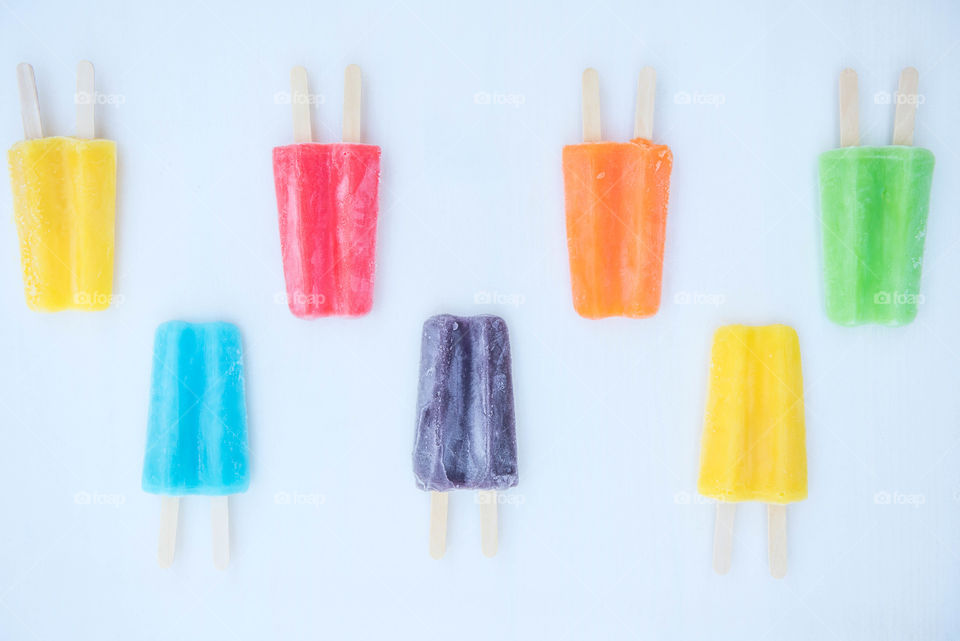 Flat lay of seven colorful frozen popsicles lined up in a pattern