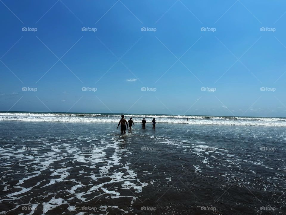 People walking across the water to reach the ocean with the blue sky as background.